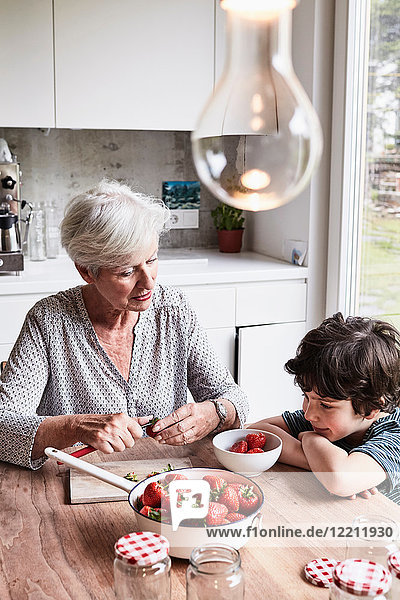 Grandmother sitting at kitchen table  preparing strawberries  grandson sitting beside her  watching