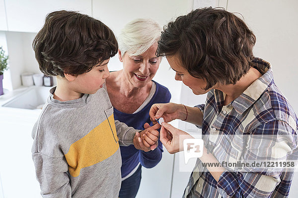 Mutter legt Gips auf den Finger des Sohnes  Großmutter hält die Hand des Enkels