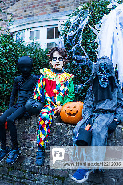 Porträt von drei Jungen in Halloween-Kostümen  an der Wand sitzend