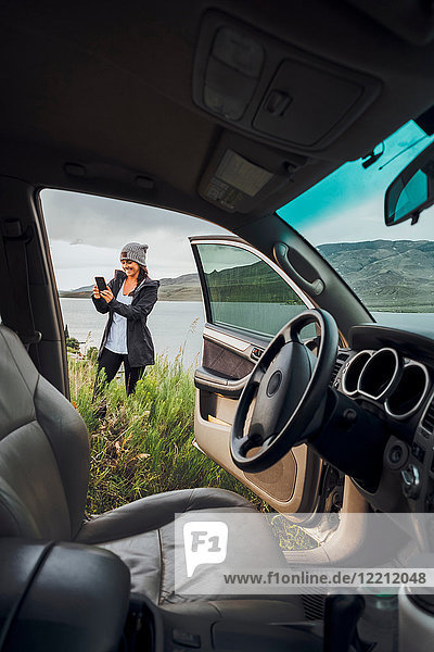 Young woman standing beside Dillon Reservoir  holding smartphone  view through parked car  Silverthorne  Colorado  USA