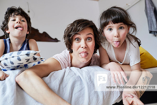 Portrait of mother  son and daughter  lying on bed  poking tongue out