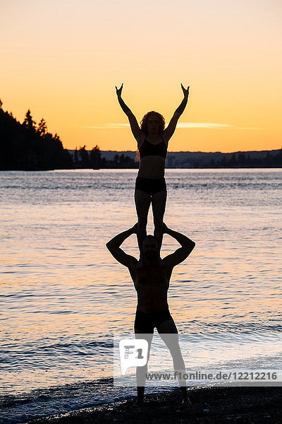Ehepaar praktiziert Yoga am Strand bei Sonnenuntergang