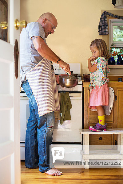 Mädchen auf dem Hocker beobachtet Vater beim Verquirlen von Essen in der Küche