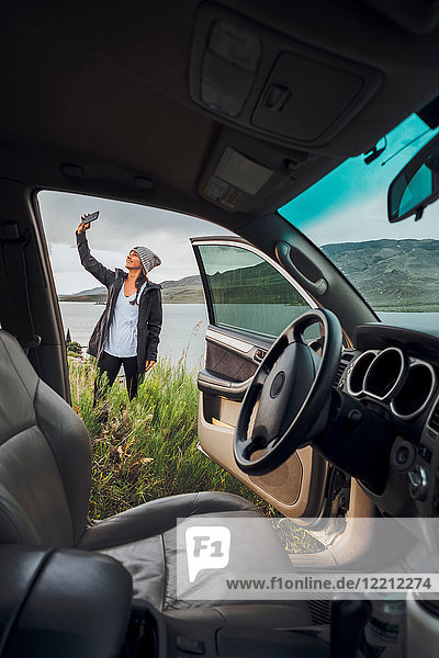 Young woman standing beside Dillon Reservoir  holding smartphone  view through parked car  Silverthorne  Colorado  USA