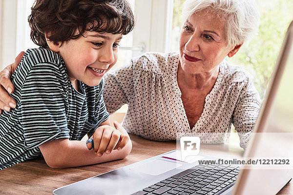 Großmutter und Enkel am Tisch sitzend  mit Laptop