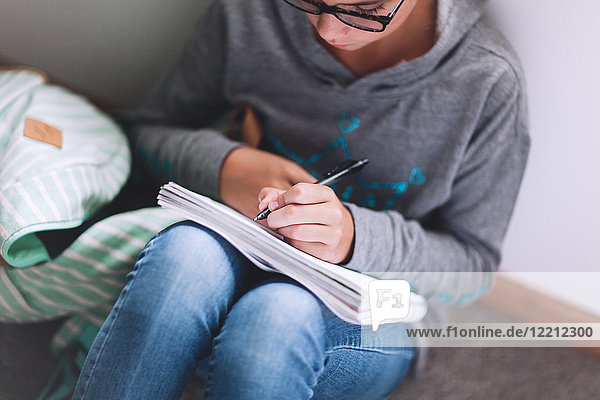 Mädchen sitzt auf dem Boden und schreibt Hausaufgaben