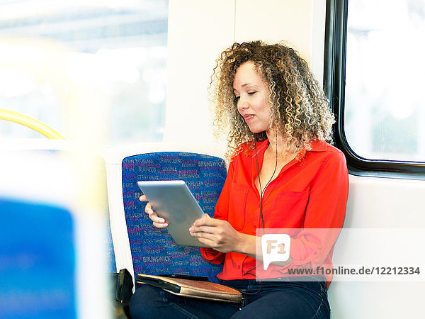 Mittlere erwachsene Frau im Zug  die ein digitales Tablet benutzt