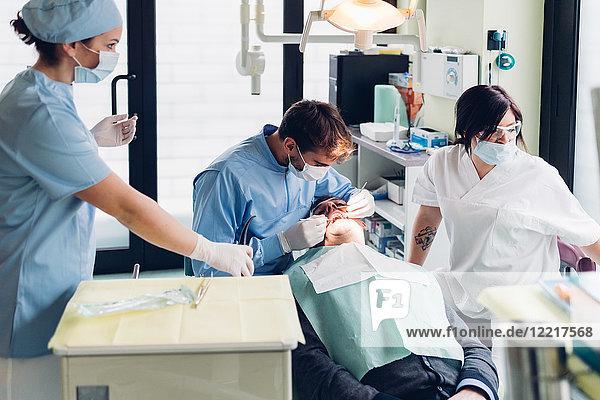 Zahnarzt schaut in den Mund des männlichen Patienten  Zahnarzthelferinnen bereiten Ausrüstung vor