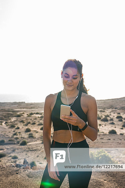 Junge Läuferin betrachtet Smartphone in trockener Küstenlandschaft  Las Palmas  Kanarische Inseln  Spanien