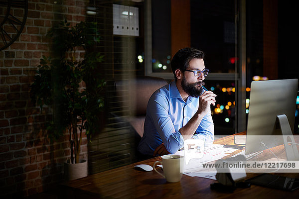 Young businessman looking at computer on office desk at night