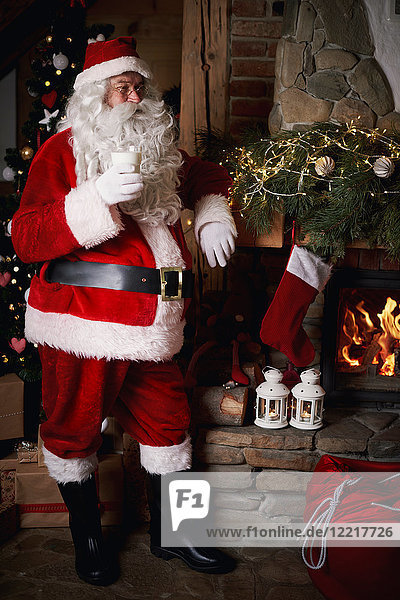 Der Weihnachtsmann steht neben dem Kamin und hält ein Glas Milch