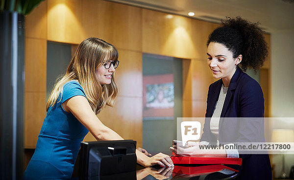 Zwei Geschäftsfrauen schauen auf Smartphone im Büroempfang
