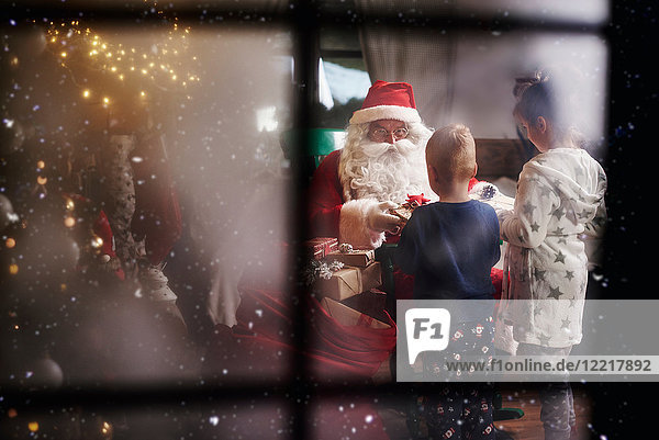 Mädchen und Junge erhalten Geschenke vom Weihnachtsmann  durch ein Fenster betrachtet