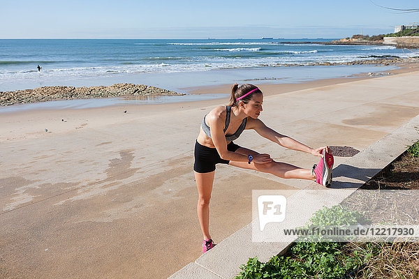 Young woman warming up on beach  stretching legs  Carcavelos  Lisboa  Portugal  Europe