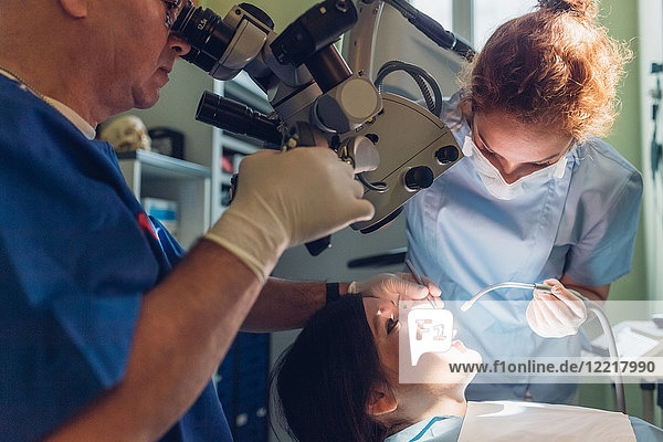Zahnarzt und Zahnarzthelferin  die einen zahnärztlichen Eingriff an einer Patientin vornehmen