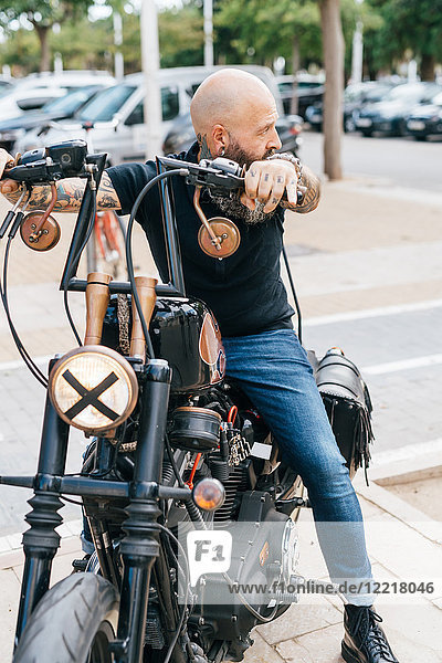 Ein reifer männlicher Hipster rittlings auf einem Motorrad  der über seine Schulter schaut