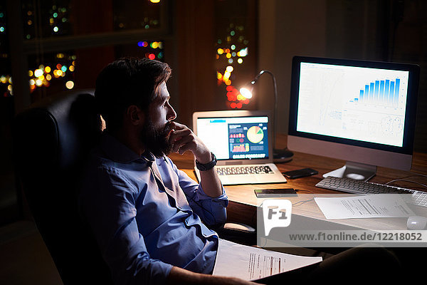 Junger Geschäftsmann starrt nachts auf Computer auf Büroschreibtisch