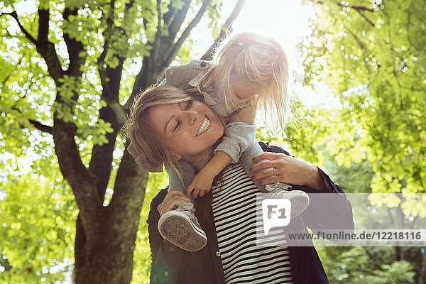 Mutter gibt Kleinkind Tochter Schulter tragen im sonnenbeschienenen Park