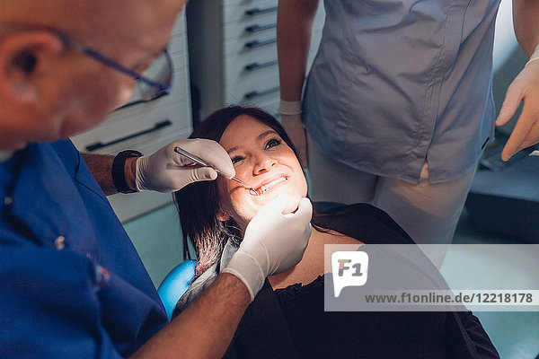 Zahnarzt und Zahnarzthelferin  die einen zahnärztlichen Eingriff an einer Patientin vornehmen