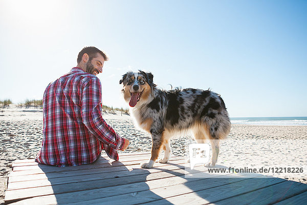 Mann sitzt mit Hund an der Strandpromenade