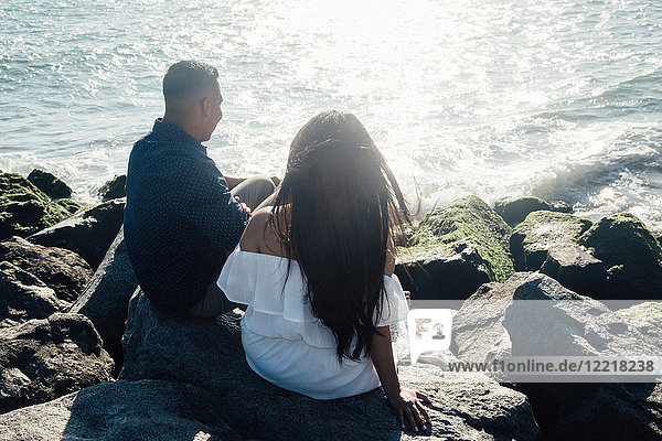 Paar auf Küstenfelsen sitzend  Blick auf Ansicht  Rückansicht