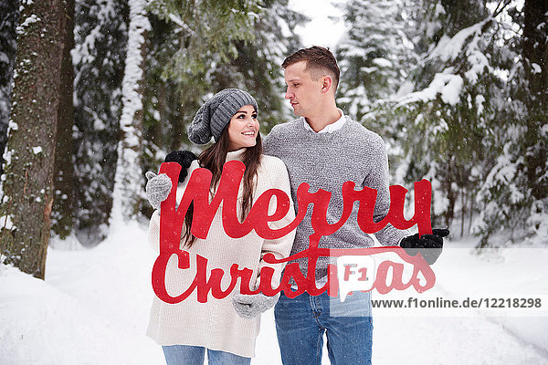 Young couple with Merry Christmas words in snow