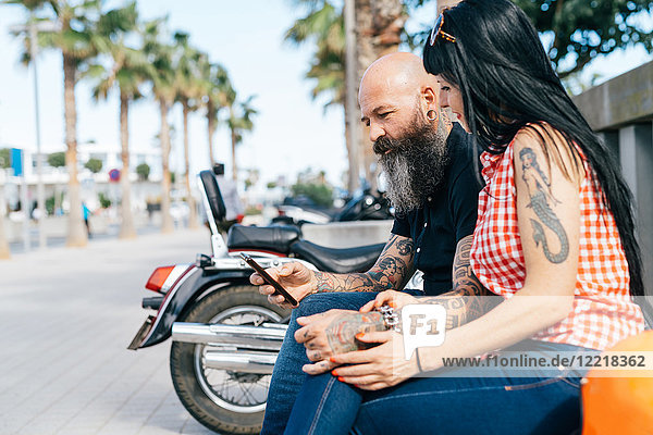 Älteres Hipster-Pärchen auf der Bank beim Betrachten eines Smartphones  Valencia  Spanien