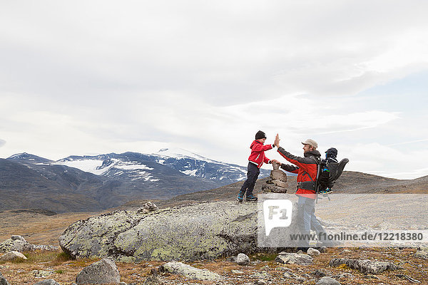 Mann mit Söhnen über einem Steinhaufen in einer Berglandschaft  Jotunheimen-Nationalpark  Lom  Oppland  Norwegen