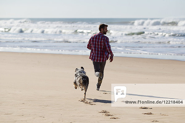 Mann rennt mit Hund am Strand