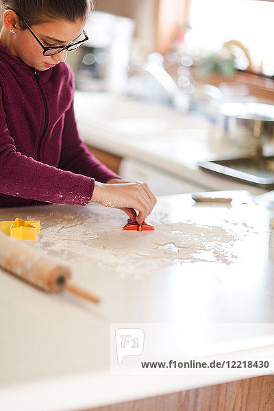 Girl using cookie cutter on dough at kitchen counter