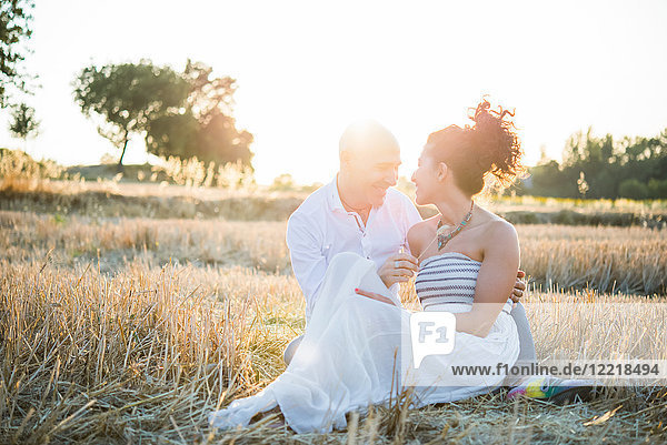 Heterosexual couple sitting in field  face to face  smiling
