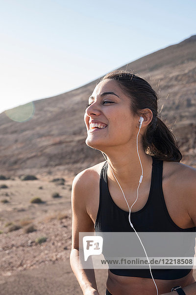 Glückliche junge Läuferin lauscht mit Kopfhörern in trockener Landschaft