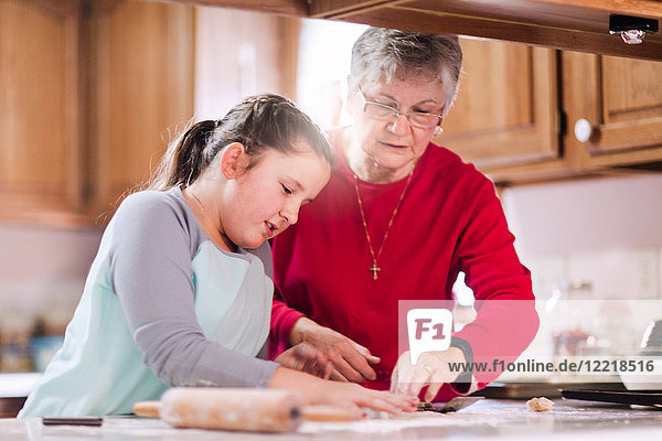 Mädchen und Großmutter mit Ausstecher auf Teig an der Küchentheke
