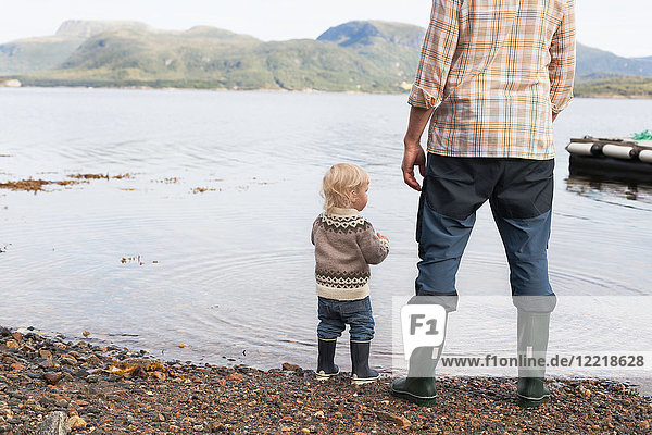 Kleinkind und Vater am Ufer des Fjords mit Blick nach draußen  Aure  More og Romsdal  Norwegen