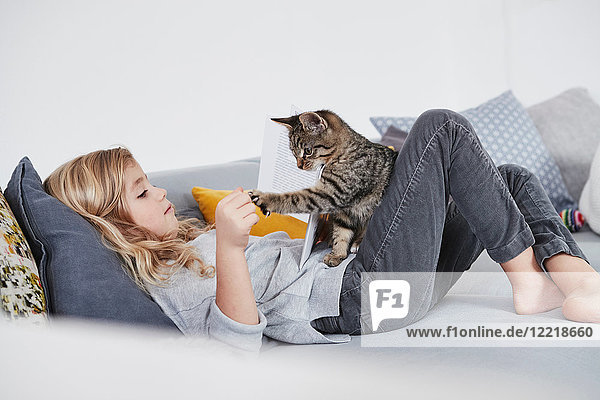 Young girl lying on sofa  playing with pet cat