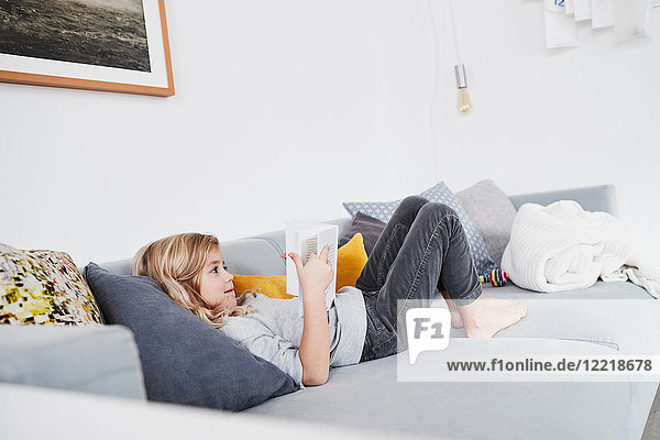 Young girl lying on sofa  reading book