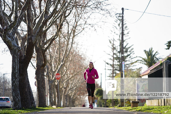 Junge Frau joggt in baumgesäumter Straße