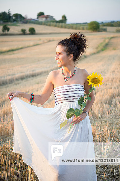 Bildnis einer mittelgroßen erwachsenen Frau  im Feld stehend  Sonnenblume haltend