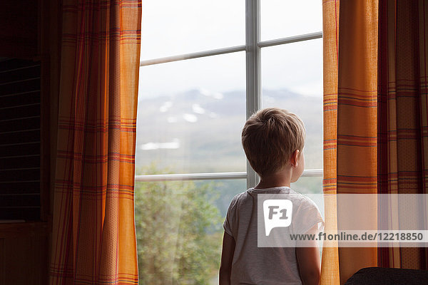 Junge schaut durch ein vorgehängtes Fenster