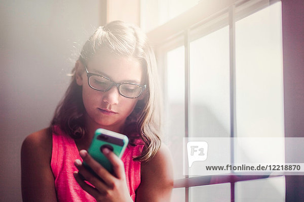 Young girl wearing glasses  beside window  using smartphone