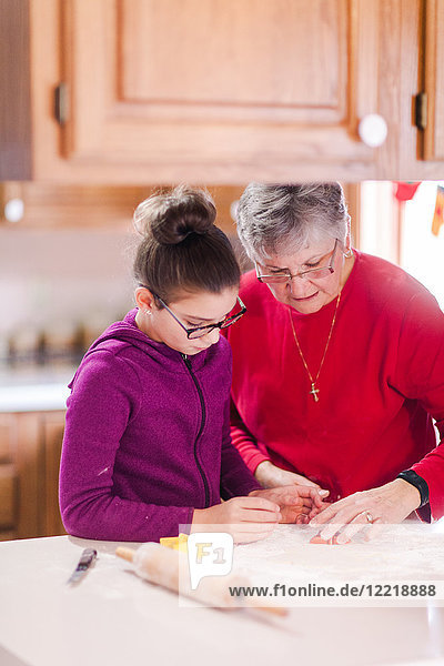 Girl and grandmother using cookie cutter on dough at kitchen counter
