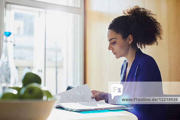 Junge Geschäftsfrau liest Papierkram am Büroschreibtisch
