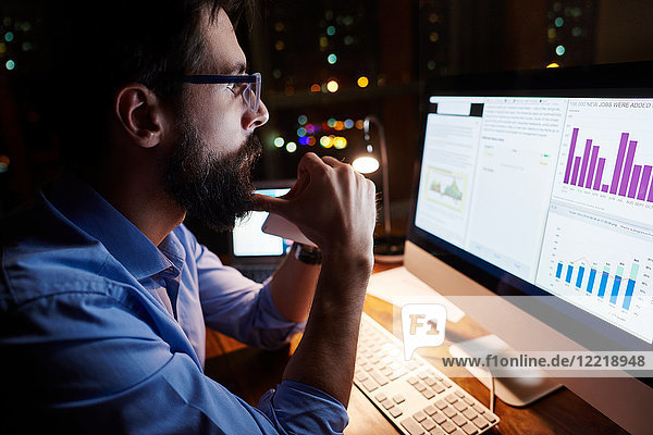 Young businessman looking at computer on office desk at night