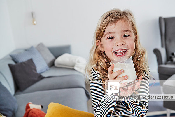 Portrait of young girl sitting in living room  holding glass of milk  smiling