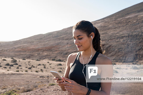 Junge Läuferin betrachtet Smartphone in trockener Landschaft  Las Palmas  Kanarische Inseln  Spanien