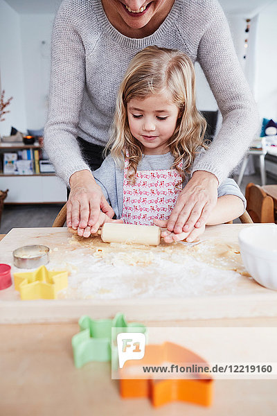 Mother helping daughter roll out cookie dough on kitchen table  mid section