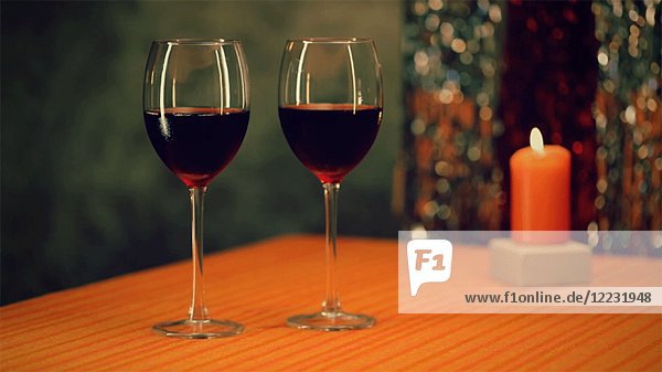 Zwei Gläser Rotwein auf dem Tisch mit Orange Kerze im Hintergrund