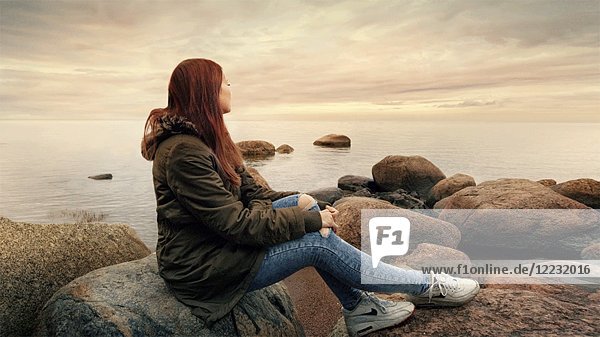 Junge Frau sitzt auf einem Felsen am Rande des Wassers