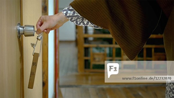 Frau in traditioneller japanischer Kleidung entriegelt Tür mit Schlüssel
