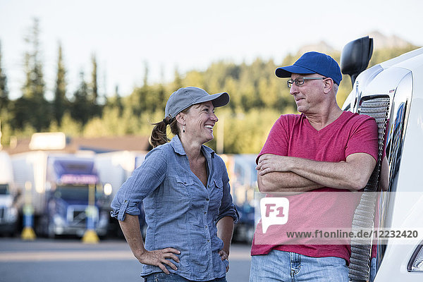 Ein kaukasisches Fahrerteam aus Mann und Frau im Gespräch vor einem großen Lastwagen an einem Truckstop.